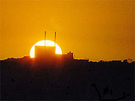Scenic picture of a sunset with the Sun close to the horizon and partly obscured by a building with two tall chimneys